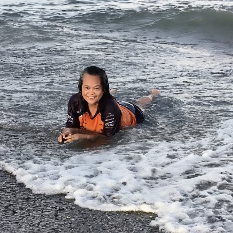 Bernadette lying on the shoreline as gentle waves wash over her, resting in a quiet moment of freedom.